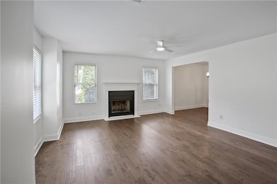 Unfurnished living room featuring a fireplace with raised hearth, dark wood finished floors, and ceiling fan