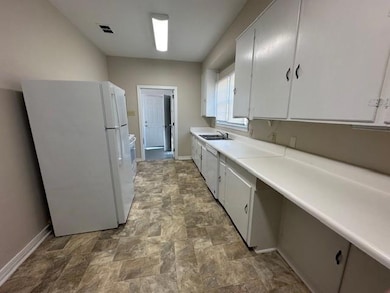 Kitchen featuring white appliances, baseboards, stone finish floors, and a sink