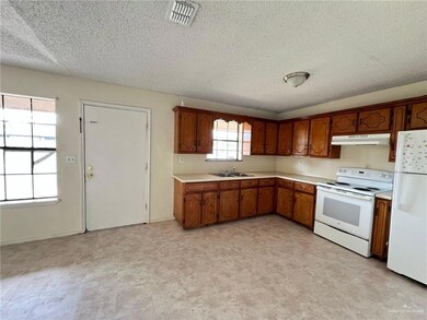 Kitchen featuring white appliances, under cabinet range hood, brown cabinetry, light countertops, and light floors