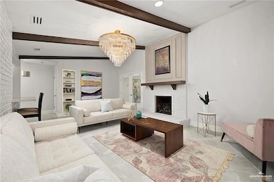 Living room with beamed ceiling, a brick fireplace, a chandelier, and built in shelves