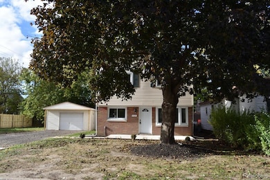 View of property hidden behind natural elements featuring an outbuilding, brick siding, a detached garage, and driveway