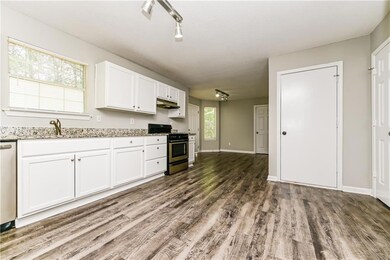 Kitchen with appliances with stainless steel finishes, wood finished floors, track lighting, white cabinetry, and under cabinet range hood
