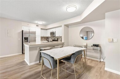 Kitchen featuring appliances with stainless steel finishes, a textured ceiling, a peninsula, white cabinets, and light wood-type flooring