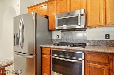 Kitchen with stainless steel appliances, tasteful backsplash, brown cabinetry, and light stone countertops