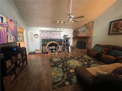 Living room with vaulted ceiling, a fireplace, a ceiling fan, wood-type flooring, and a textured ceiling