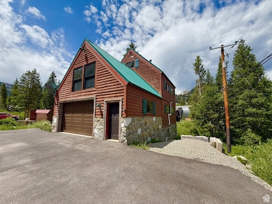 Rustic home with asphalt driveway, stone siding, a garage, and a metal roof