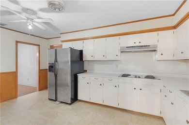 Kitchen featuring ornamental molding, wallpapered walls, wainscoting, stainless steel fridge with ice dispenser, and light countertops