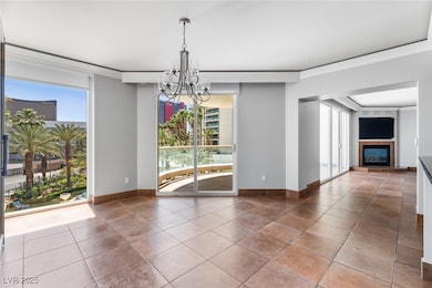 Tiled spare room featuring a chandelier, a tiled fireplace, ornamental molding, and baseboards