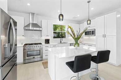 Kitchen with stainless steel appliances, wall chimney range hood, backsplash, light wood finished floors, and light countertops