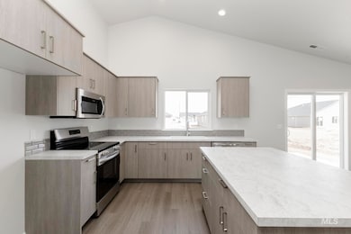 Kitchen with light brown cabinets, stainless steel appliances, light countertops, recessed lighting, and high vaulted ceiling
