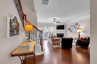 Living area featuring ceiling fan, stairway, a glass covered fireplace, dark wood-type flooring, and ornamental molding