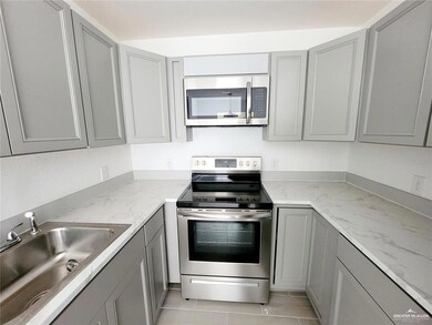 Kitchen with appliances with stainless steel finishes, gray cabinets, a sink, light tile patterned floors, and light stone countertops
