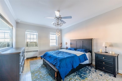 Bedroom with ornamental molding, wood finished floors, radiator, ceiling fan, and cooling unit