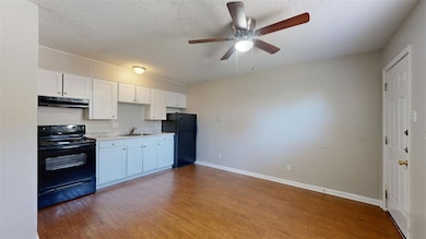 Kitchen with black appliances, dark wood-style floors, white cabinetry, light countertops, and a textured ceiling