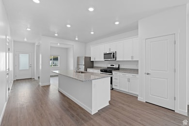 Kitchen featuring white cabinets, a center island with sink, wood finished floors, and stainless steel appliances