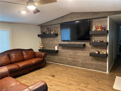 Living room with wood finished floors, lofted ceiling, ceiling fan, and wooden walls