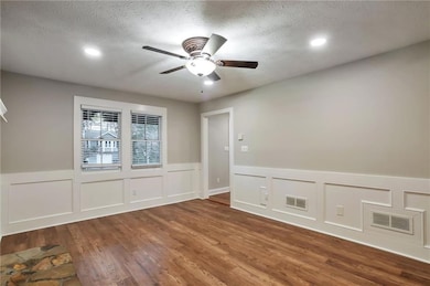 Unfurnished room with a decorative wall, wainscoting, a textured ceiling, wood finished floors, and ceiling fan