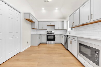 Kitchen featuring appliances with stainless steel finishes, vaulted ceiling, gray cabinets, light wood-style floors, and decorative backsplash