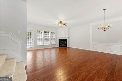 Living room featuring a ceiling fan, a chandelier, wood finished floors, a glass covered fireplace, and a wainscoted wall