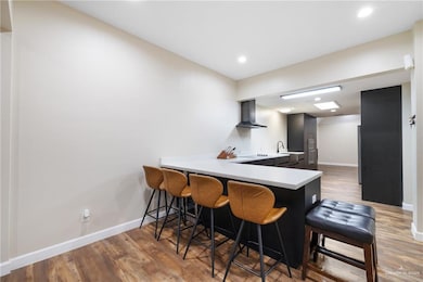 Kitchen with a peninsula, light countertops, a kitchen breakfast bar, light wood-style floors, and wall chimney range hood