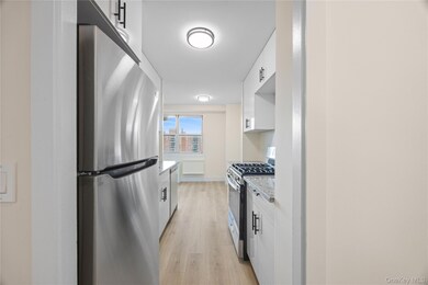 Kitchen featuring stainless steel appliances, white cabinetry, light wood-type flooring, and light stone counters