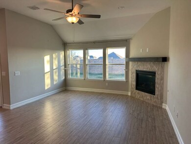 Unfurnished living room with wood finished floors, vaulted ceiling, a tiled fireplace, and a ceiling fan