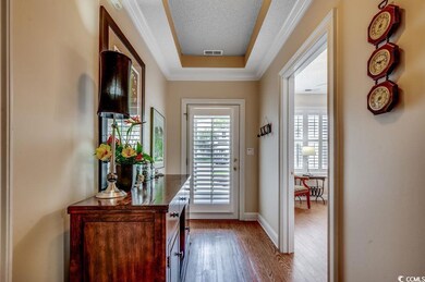 Doorway to outside featuring wood finished floors, a tray ceiling, and ornamental molding