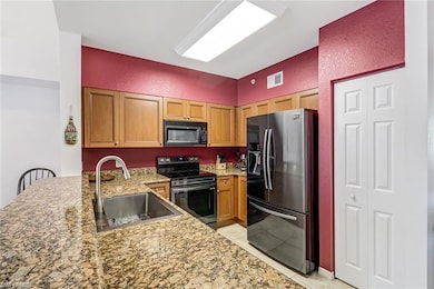 Kitchen featuring a peninsula, stainless steel appliances, a textured wall, light stone counters, and light tile patterned floors