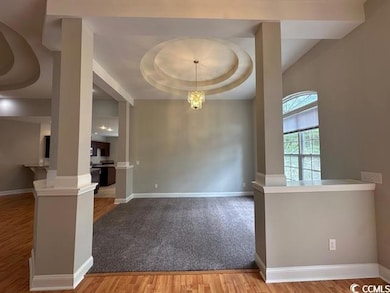 Unfurnished dining area with light wood-style floors, a raised ceiling, a chandelier, and decorative columns