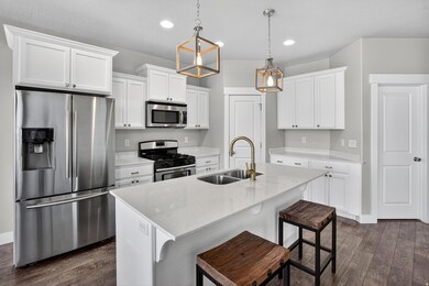 Kitchen with appliances with stainless steel finishes, a kitchen breakfast bar, dark wood-style flooring, light stone counters, and a center island with sink