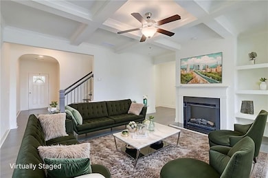 Living area with coffered ceiling, arched walkways, beam ceiling, a ceiling fan, and a fireplace
