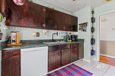 Kitchen with white dishwasher, dark countertops, light tile patterned floors, and dark brown cabinetry