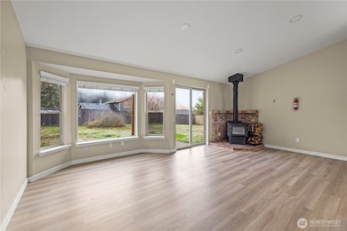 Spacious living room with large bay windows, sliding glass door to backyard, and a brick-faced wood stove for cozy evenings. Open layout ideal for entertaining or relaxing at home.