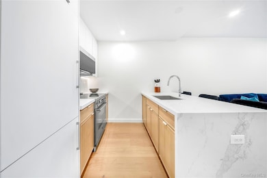 Kitchen featuring a peninsula, light wood-type flooring, stainless steel appliances, light stone counters, and white cabinets