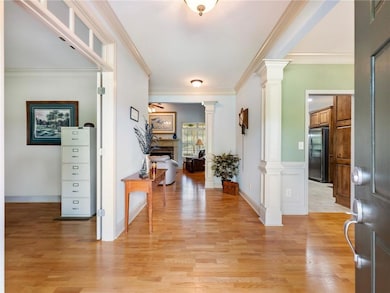 Foyer featuring ornate columns, a fireplace, light wood-type flooring, and ornamental molding