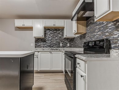 Kitchen with black electric range, backsplash, and white cabinets