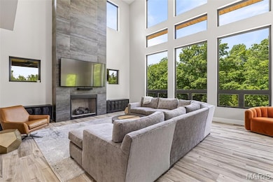Living area featuring a high ceiling, light wood-type flooring, and a tiled fireplace