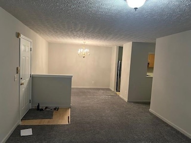 Hall featuring dark colored carpet, a chandelier, and a textured ceiling