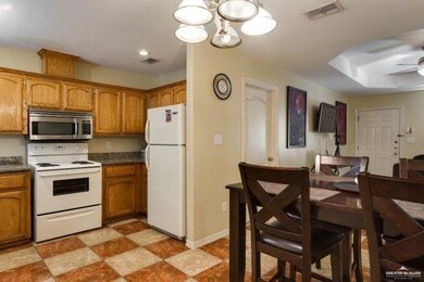 Kitchen featuring ceiling fan with notable chandelier, visible vents, brown cabinets, and white appliances