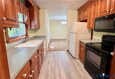 Kitchen featuring black appliances, light countertops, a chandelier, brown cabinetry, and light wood-type flooring