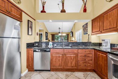 Kitchen with stainless steel appliances, a sink, dark stone counters, brown cabinetry, and hanging light fixtures