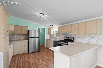 Kitchen with cream cabinetry, a peninsula, dark wood-style floors, stainless steel appliances, and light countertops