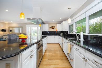 Kitchen with brand new appliances, white cabinetry, ornamental molding, backsplash, and maple wood finished floors.