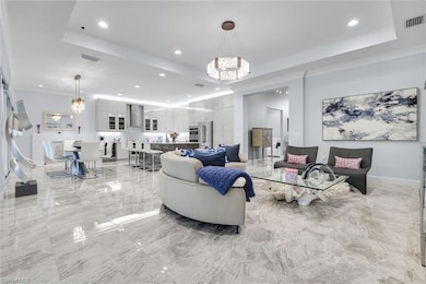 Living area featuring a chandelier, light marble finish floors, recessed lighting, and a tray ceiling