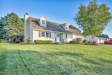 Cape cod house featuring a chimney, a front yard, an attached garage, and a shingled roof