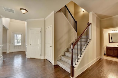 Entrance foyer with dark wood-style floors, ornamental molding, and stairway