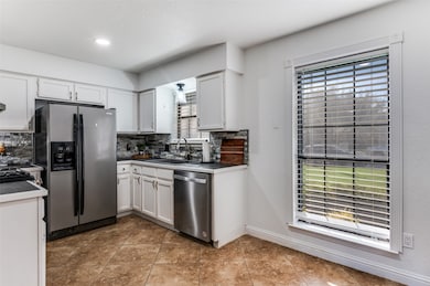 Kitchen with white cabinets, appliances with stainless steel finishes, tasteful backsplash, light tile patterned floors, and dark countertops