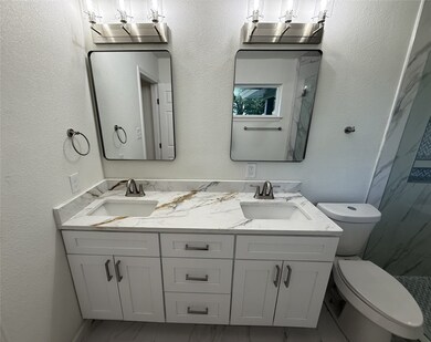 Primary bathroom featuring a textured wall, double vanity, marble finish floors, and a marble finish shower
