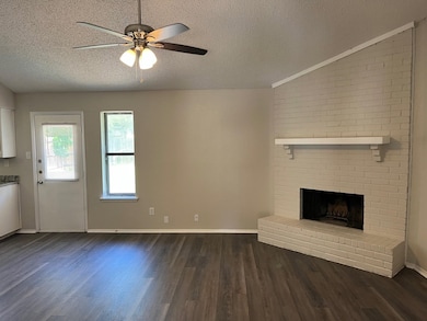 Unfurnished living room featuring dark wood finished floors, a textured ceiling, a fireplace, and a ceiling fan