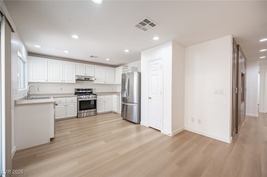 Kitchen featuring appliances with stainless steel finishes, white cabinets, light countertops, light wood-type flooring, and recessed lighting